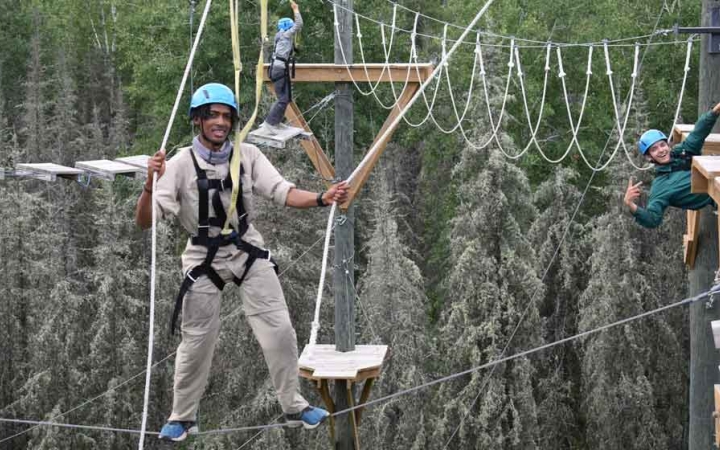 two students are suspended by ropes as they make their way through a ropes course on an outward bound expedition